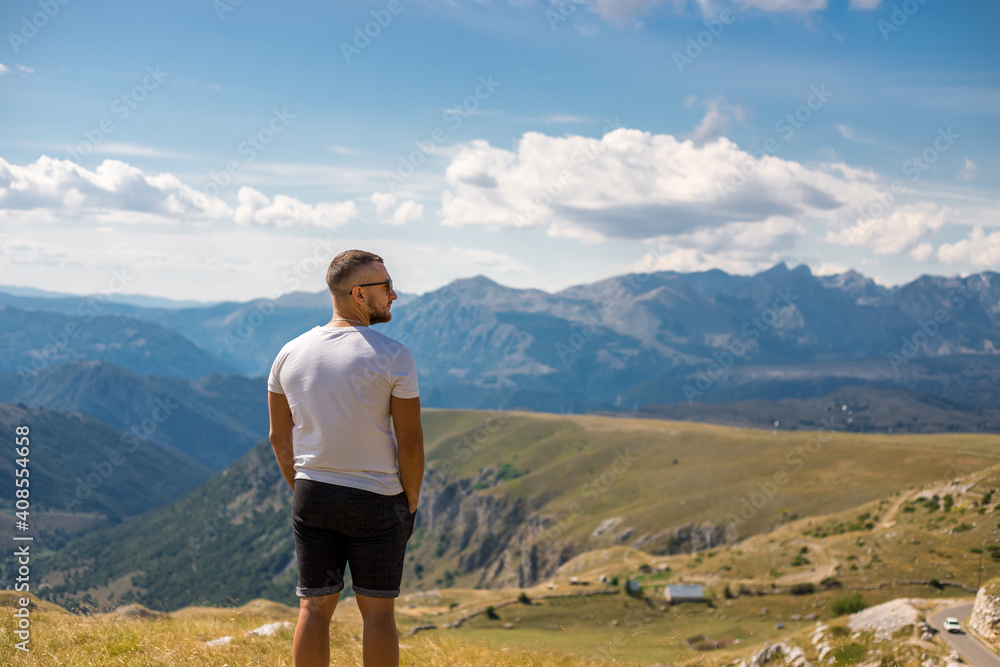 Young man standing on top of cliff in summer mountains enjoying view of nature.