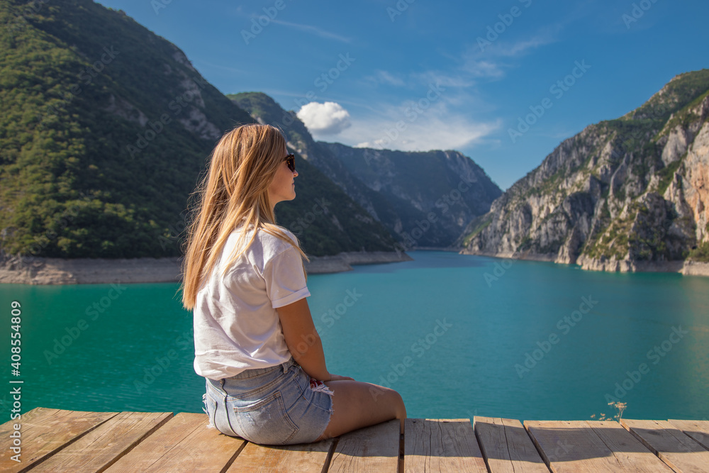 Young woman sitting on wooden pier at Piva lake, Montenegro.