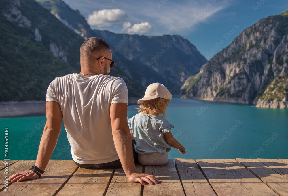 Father and little daughter sitting on a wooden pier at Piva lake.