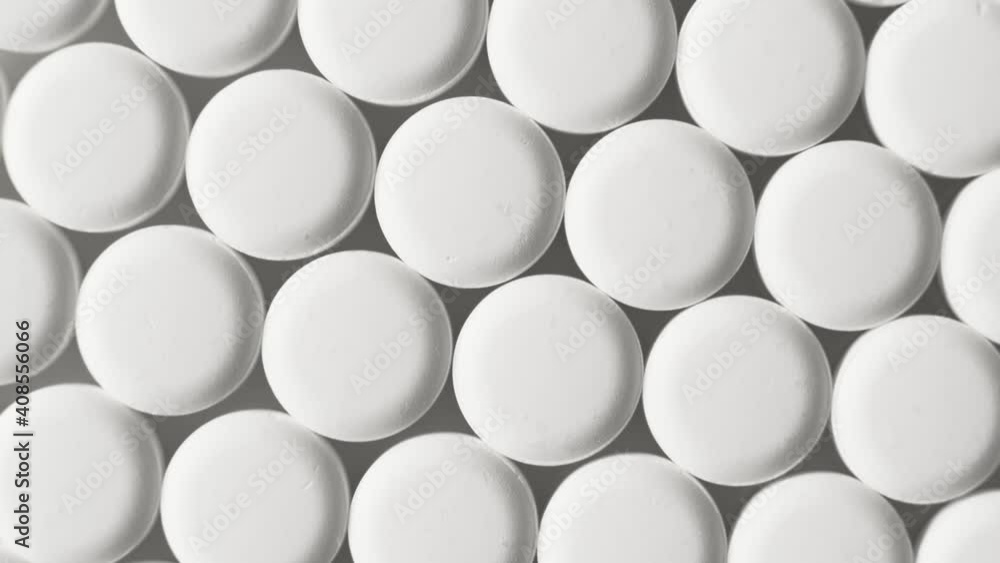 White pills on the conveyor, pharmaceutical factory, top view, rotate. Antiviral drugs, virus protection, Covid-19 treatment. White pills on the conveyor, pharmaceutical factory, top view, rotate. Antiviral drugs, virus protection, Covid-19 treatment.