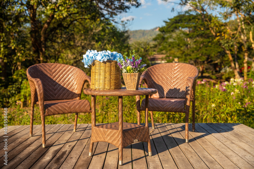 Two armchairs, wooden garden furniture on wood floor outdoor for relaxing on hot summer days. Garden landscape with two chairs in nature, flowers in vase and cat. Rest in park cafe. Backyard exterior Two armchairs, wooden garden furniture on wood floor outdoor for relaxing on hot summer days. Garden landscape with two chairs in nature, flowers in vase and cat. Rest in park cafe. Backyard exterior
