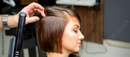 A male hairdresser is straightening the hair of the young woman in a beauty salon