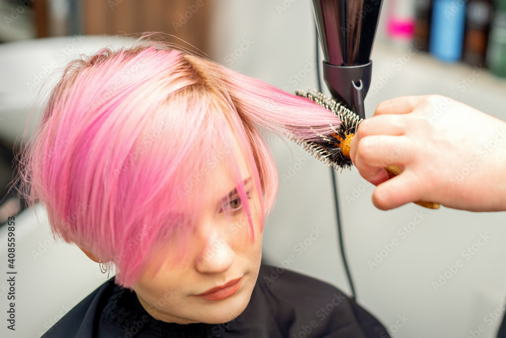 Naklejka premium Hairdresser dries pink hair of the young woman in a beauty salon
