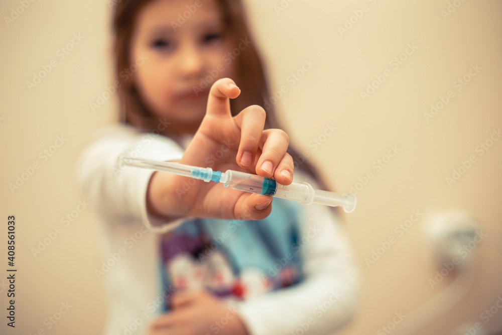 Little girl holding a syringe with a liquid inside. Concept fight against virus covid-19 corona virus. Little girl holding a syringe with a liquid inside. Concept fight against virus covid-19 corona virus.