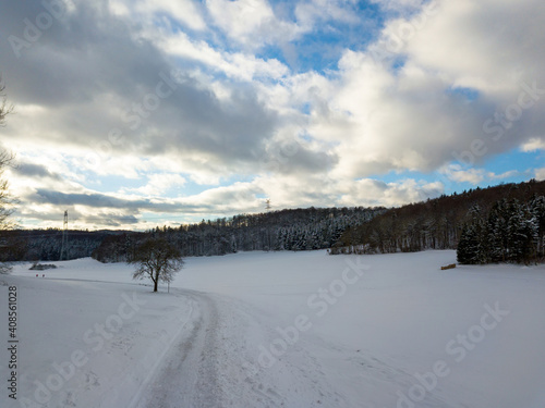 Aerial view on winter landscape with trees in forest covered with hoarfrost and people walking through snow covered paths agains great blue sky with clouds