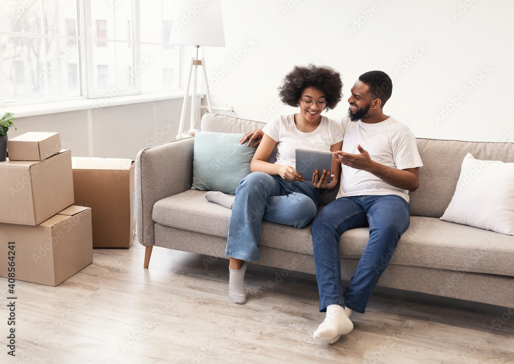 Happy Black Spouses Using Tablet Sitting Among Moving Boxes Indoor