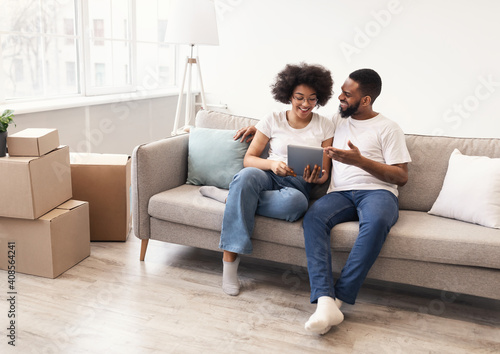 Happy Black Spouses Using Tablet Sitting Among Moving Boxes Indoor
