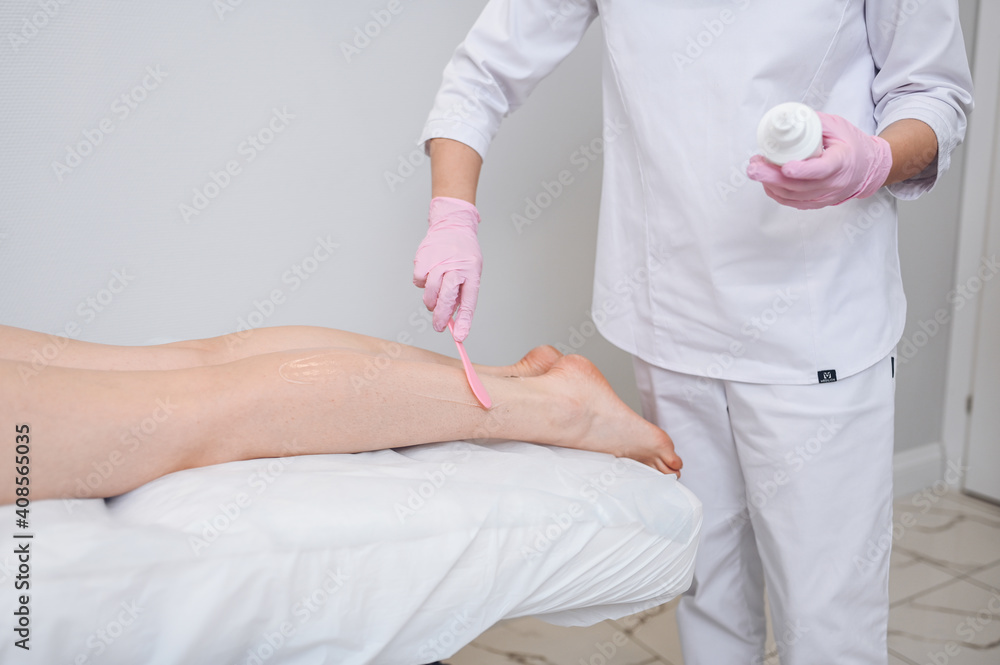 Laser epilation and cosmetology in beauty salon, spa concept. Preparation for the procedure of laser hair removal. Application of gel, disposable spatula. Beautiful smooth female legs. Laser epilation and cosmetology in beauty salon, spa concept. Preparation for the procedure of laser hair removal. Application of gel, disposable spatula. Beautiful smooth female legs.