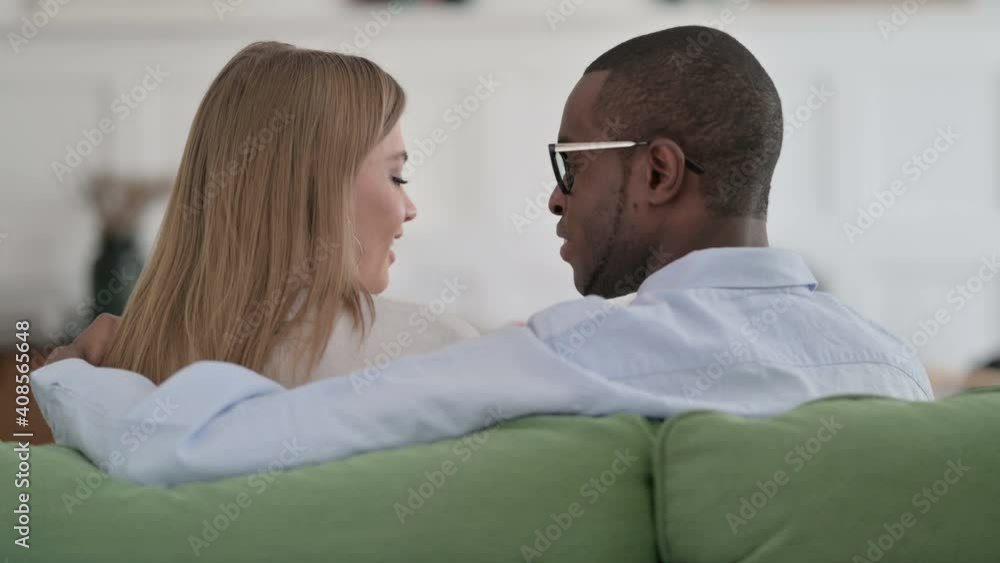 Rear View of Loving Mixed Race Couple Talking While Sitting on Sofa Rear View of Loving Mixed Race Couple Talking While Sitting on Sofa