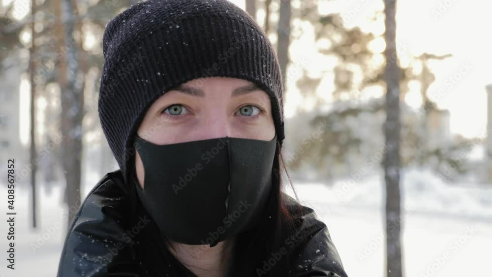 Portrait of a young woman in a black mask stands in the city in the winter. Woman wearing protective medical mask outdoors over snow in winter. Health and pandemic concept. Portrait of a young woman in a black mask stands in the city in the winter. Woman wearing protective medical mask outdoors over snow in winter. Health and pandemic concept.