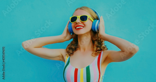 Portrait of modern happy young woman with headphones listening to music on a blue background