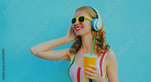 Portrait of modern happy young woman with headphones listening to music on a blue background