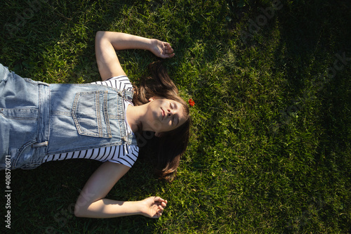 teenage girl lies with her eyes closed on green grass on a summer day photo