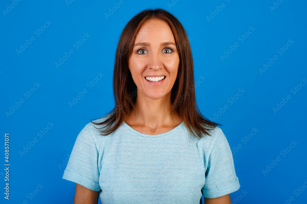 Portrait of a smiling brunette in a blue t-shirt looking at the camera, isolated on a blue background. Portrait of a smiling brunette in a blue t-shirt looking at the camera, isolated on a blue background.