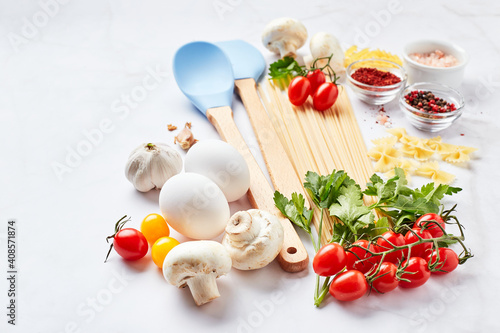 Food background with place for text, with different kinds of pasta, tomatoes, herbs, mushrooms, eggs, seasonings scattered on light marble background. Italian cuisine concept