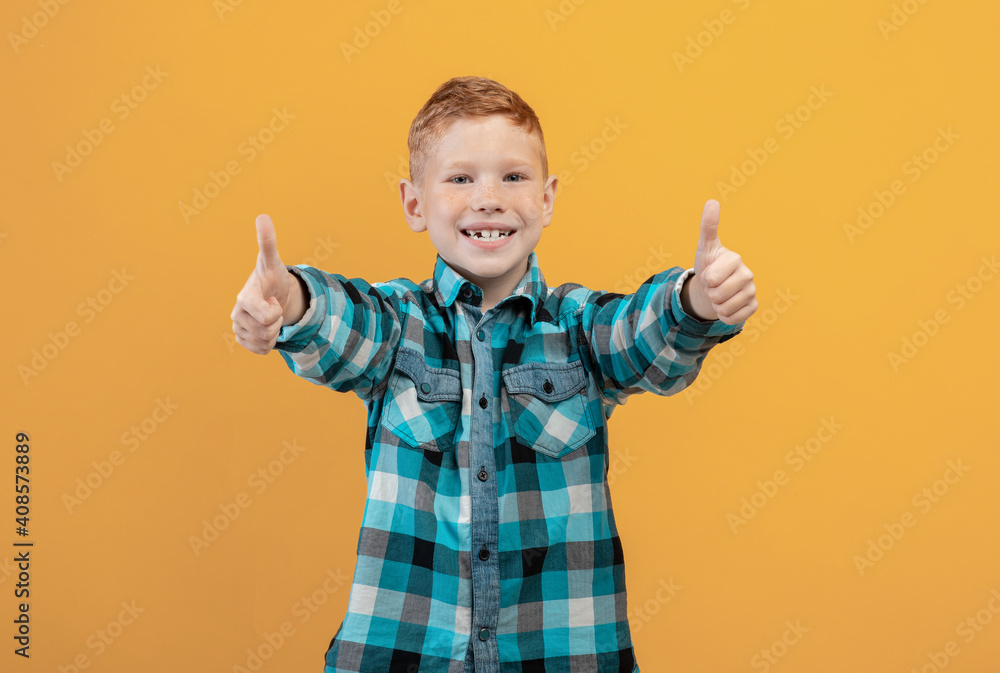 Happy ginger kid showing thumbs up on yellow studio background Happy ginger kid showing thumbs up on yellow studio background