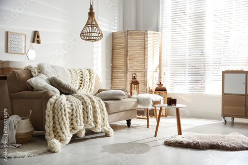Cozy living room interior with beige sofa, knitted blanket and cushions photo