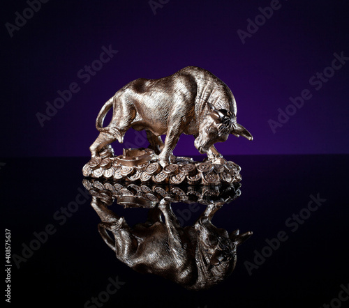 Metal bull figurine on money stand on reflective surface. A financial symbol. Year symbol. Looks like bull on handful of couns looking into black river