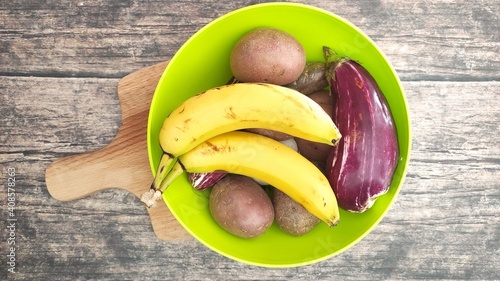 A green bowl with bananas, potatoes and eggplant