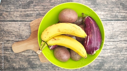 A green bowl with bananas, potatoes and eggplant