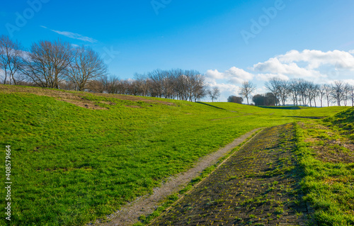 Dike in a green grassy field in wetland in sunlight under a blue sky in winter, Almere, Flevoland, The Netherlands, January 24, 2021 
