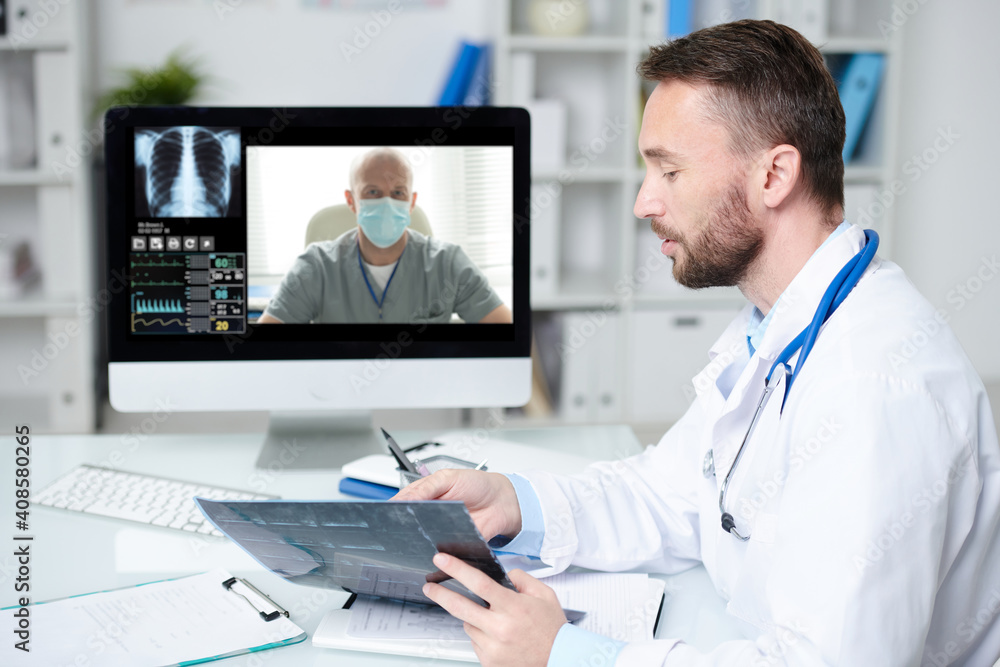 Doctor pointing at x-ray of patient during online consultation with colleague Doctor pointing at x-ray of patient during online consultation with colleague