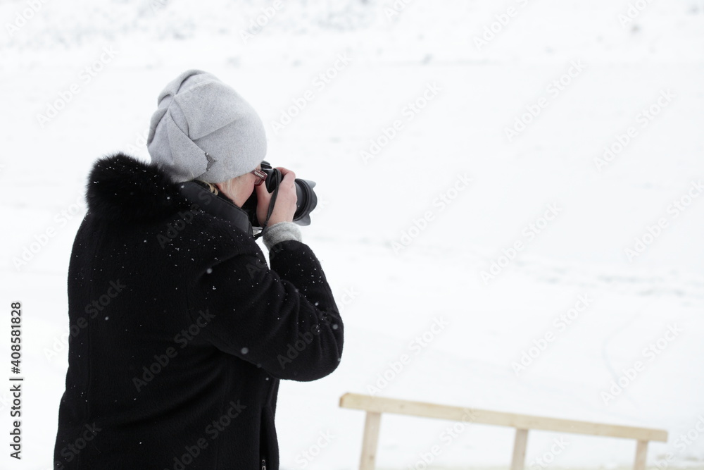 Elderly Caucasian tourist woman photographer with digital SLR camera zoom lens taking pictures of Russian winter snow landscape at cold day Elderly Caucasian tourist woman photographer with digital SLR camera zoom lens taking pictures of Russian winter snow landscape at cold day