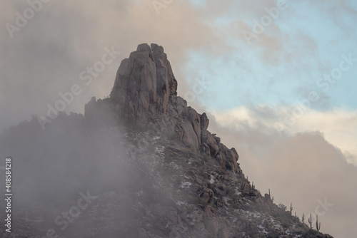 A winter storm in the desert envelopes Pinnacle Peak, Scottsdale. Snow is sprinkled in the rocks and saguaro cactus.