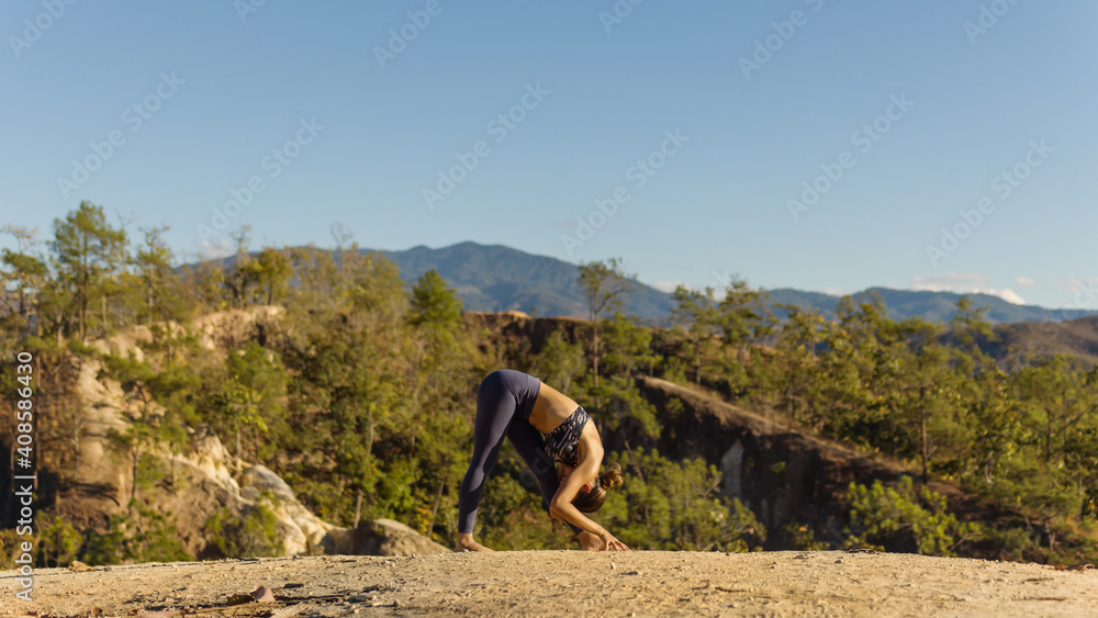 Naklejka premium Young good looking woman perform yoga pose on mountain with sun light during sunset