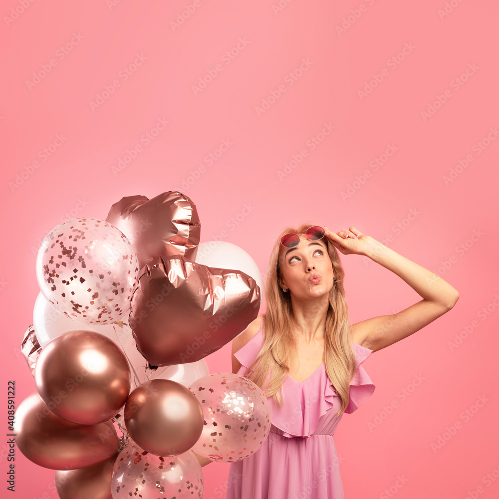 Holiday sale concept. Cute blonde woman holding bunch of balloons, pursing her lips and looking upwards at copy space Holiday sale concept. Cute blonde woman holding bunch of balloons, pursing her lips and looking upwards at copy space