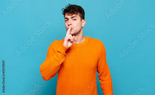 young man asking for silence and quiet, gesturing with finger in front of mouth, saying shh or keeping a secret photo