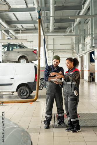Young confident technicians in workwear pointing at one of cars in workshop © pressmaster