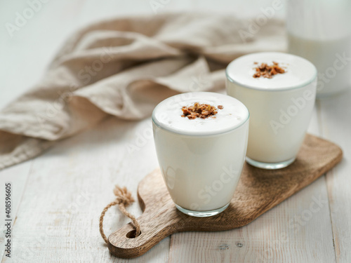 Kefir, buttermilk or yogurt with granola. Yogurt in glass on white wooden background. Probiotic cold fermented dairy drink. Gut health, fermented products, healthy gut flora concept. Copy space photo