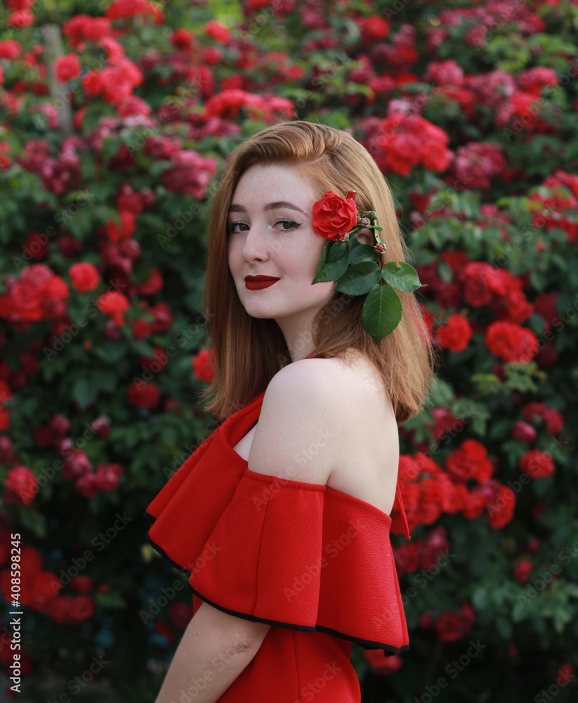 A beautiful red-haired girl in a red dress and red lips near gorgeous red roses. A beautiful red-haired girl in a red dress and red lips near gorgeous red roses.