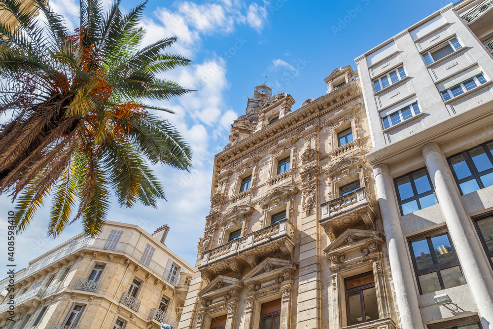 Low angle view of historical buildings and palm tree against blue cloudy sky in Toulon, France.