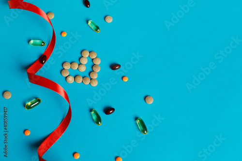 Heart of red pills decorated with a red ribbon and different vitamins on a blue background. Chelated iron  Omega-3  zinc. Valentine s Day concept  top view  flat lay