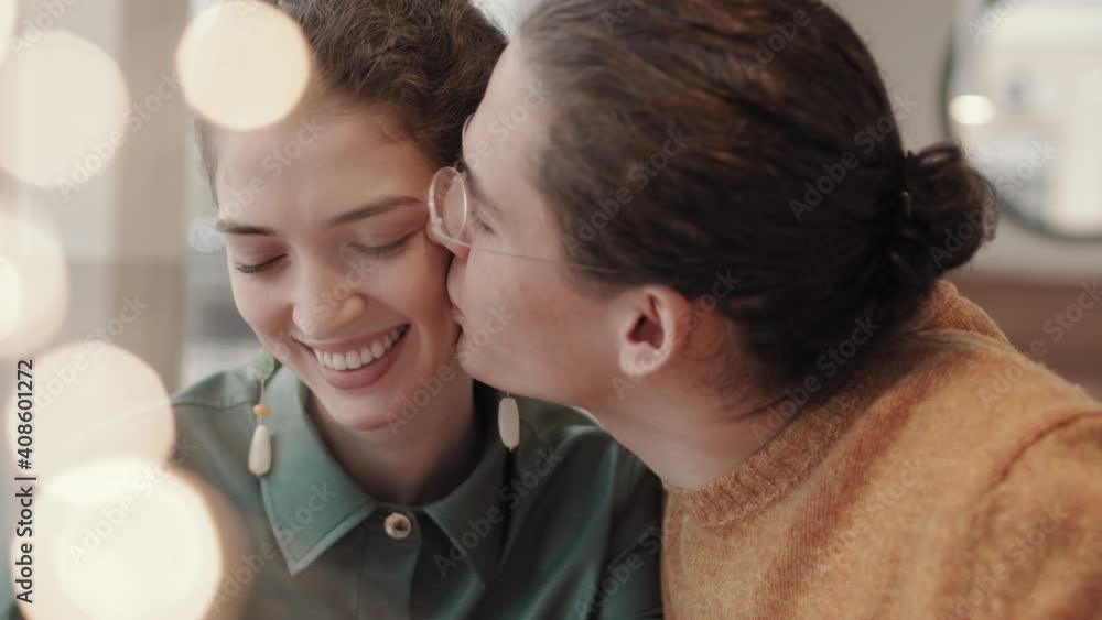 Medium shot of young attractive Caucasian woman and her handsome husband sitting in restaurant and having romantic date. Man kissing woman on cheek Medium shot of young attractive Caucasian woman and her handsome husband sitting in restaurant and having romantic date. Man kissing woman on cheek
