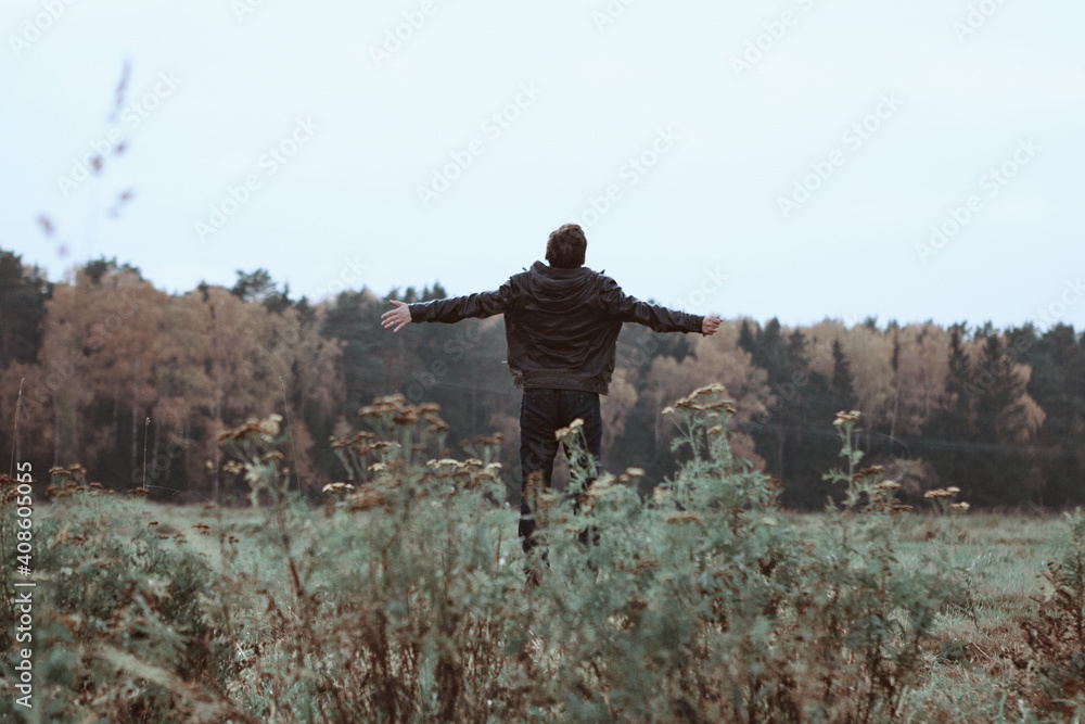 Man with arms outstretched to forest in a wild field. Freedom concept. Back view.