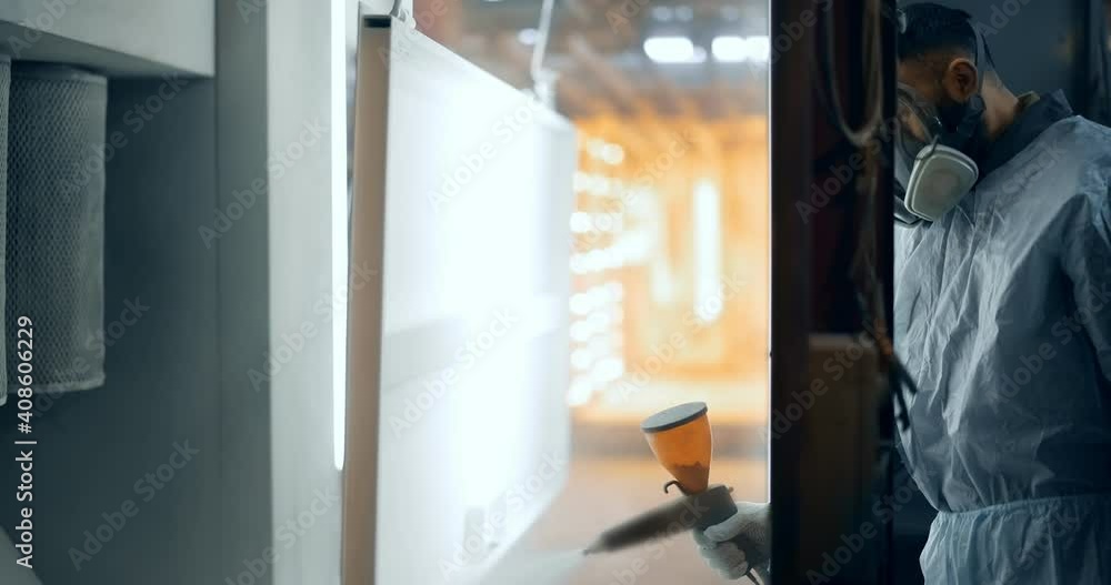 Painter in protective wear paints metal products with powder paint. Powder coating process at the manufacturing Painter in protective wear paints metal products with powder paint. Powder coating process at the manufacturing