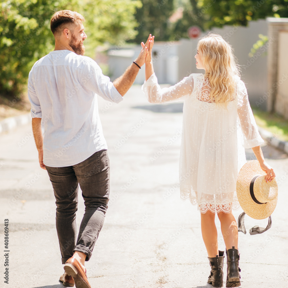 Fototapeta premium Happy and laughing man and woman holding hands walking along the road on a sunny day