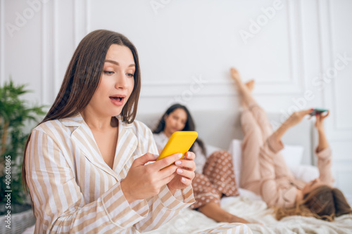 Girls with smartphones lying on bed with smartphones and looking involved