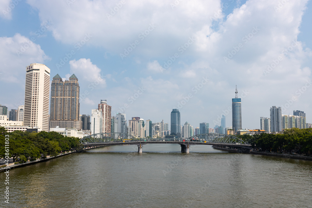 Obraz premium A bridge across the river on the banks of which there are park areas. In the background are skyscrapers and high-rise buildings. China, Guangzhou