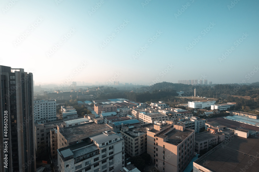 Morning in Guangzhou, China There are small and tall houses and cars on the road below. Mountains in the background. Roofs of the houses