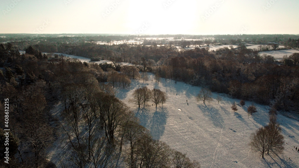Sun setting over snow covered park and wood land from aerial drone