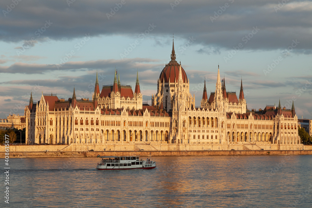Fototapeta premium The Hungarian Parliament seen from across the Danube River, on the Buda side, is reflected in the river's waters as the evening lights turn orange, Budapest.