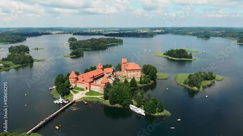 Aerial drone shot of red brick medieval castle on island in Trakai, Vilnius region, Lithuania. Sunny midday summer weather with some boats on the lake. Flying forward pitch down camera movement photo