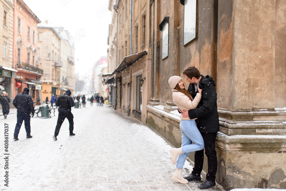 Young couple kissing under a huge pine in a city covered with white snow Young couple kissing under a huge pine in a city covered with white snow