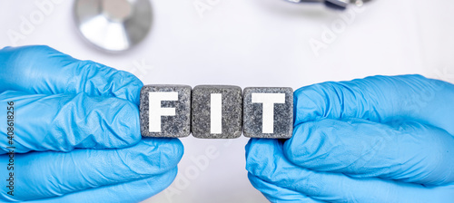 FIT - word from stone blocks with letters holding by a doctor's hands in medical protective gloves