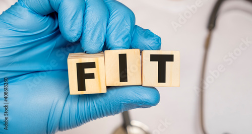 FIT - word from wooden blocks with letters holding by a doctor's hands in medical protective gloves. Medical concept.