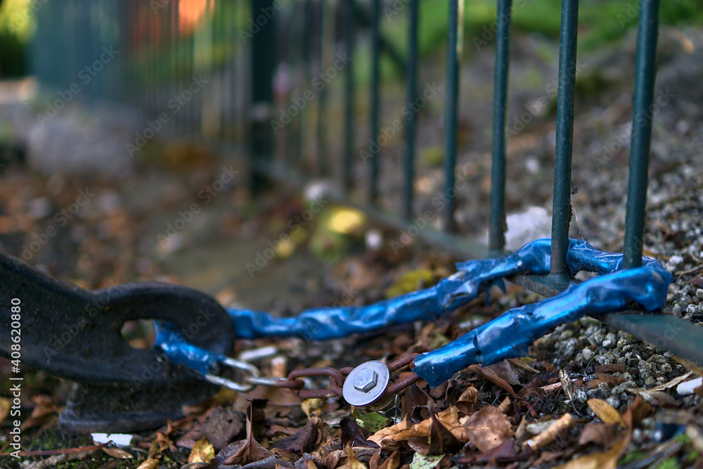 Naklejka premium Bench locked to the metal fence by chain in order to prevent movement and stealing. Seen in St Stephen Green park, Dublin, Ireland. Soft and selective focus. Focus on the chain